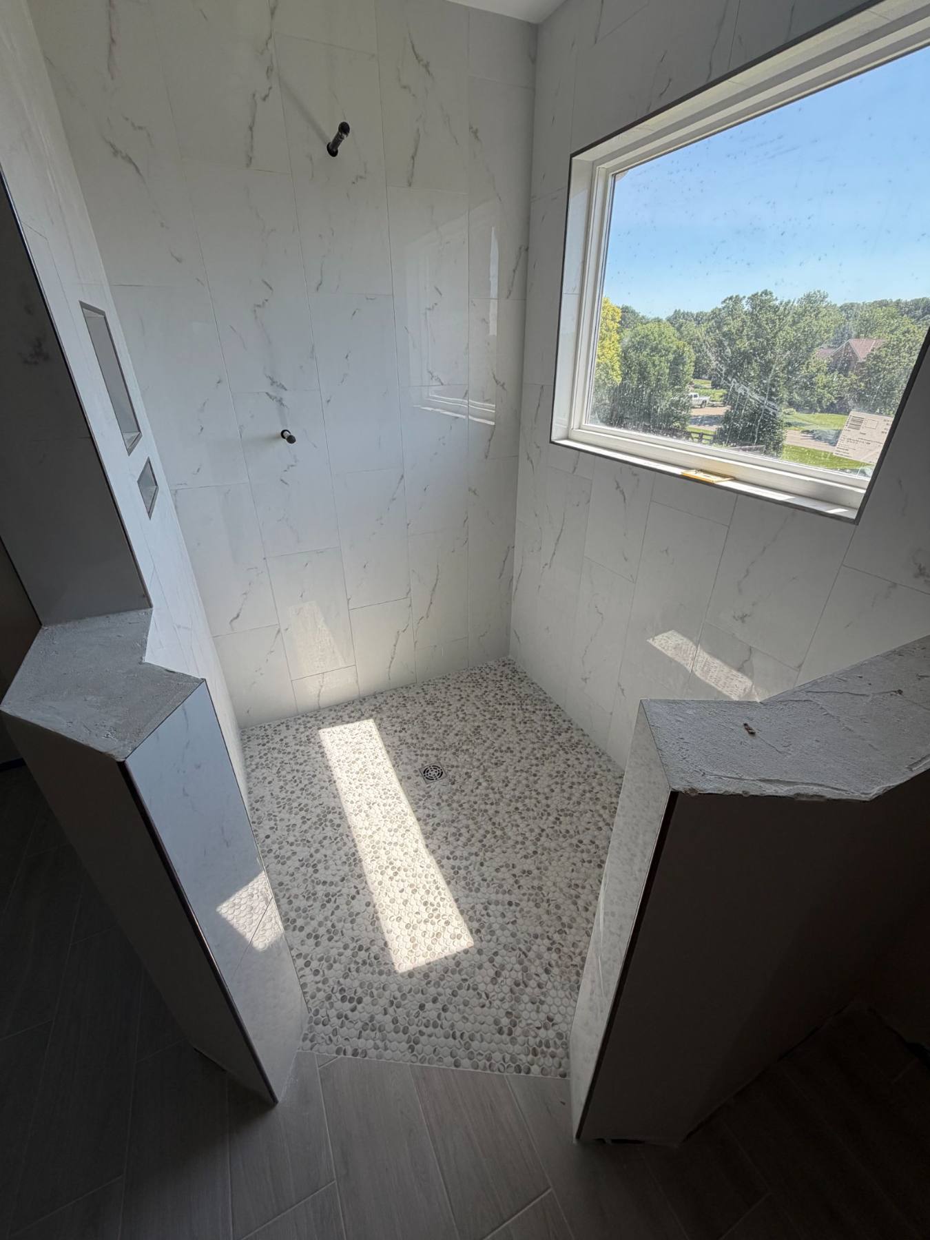 New-build marble shower with pebble floor by Resolute Construction and Remodel